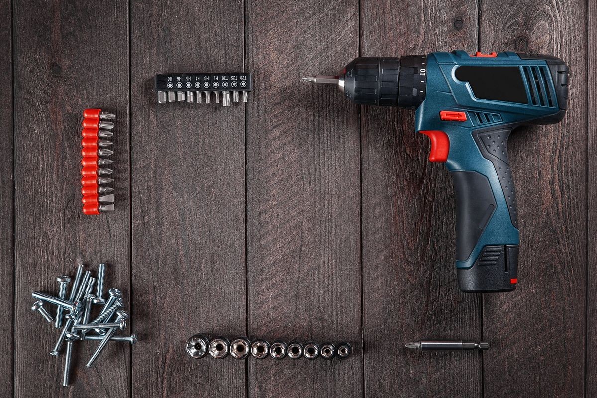 Blue electric screwdriver lies on  black wooden table with bolts and bits. Top view. Free space for text.