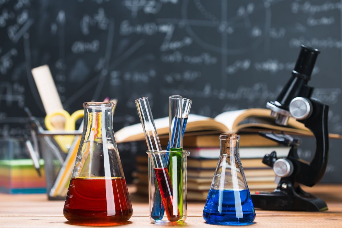 School supplies. Tubes with chemical liquids stand on a wooden table on a chalkboard background with digital formulas