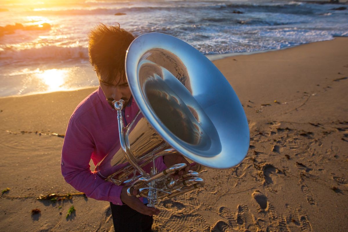 Musician playing the Tuba on the sea coast during an amazing sunset.