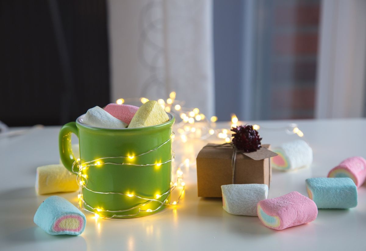 coffee cup with marshmallows and gift box for Valentine's Day on white background with fairy lights. 