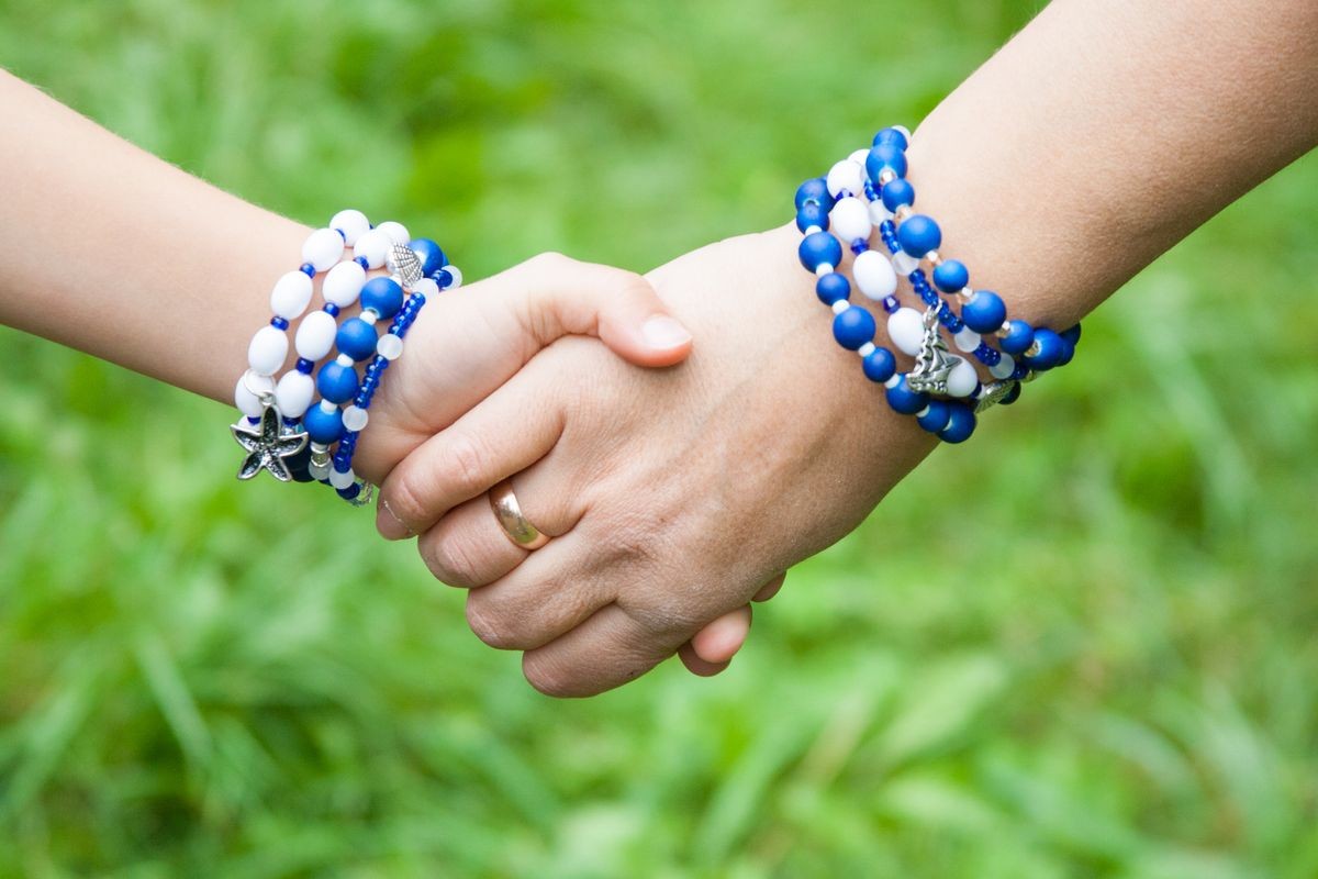 Mother holding daughter's hand. They both wear equal sea style handmade bracelets.