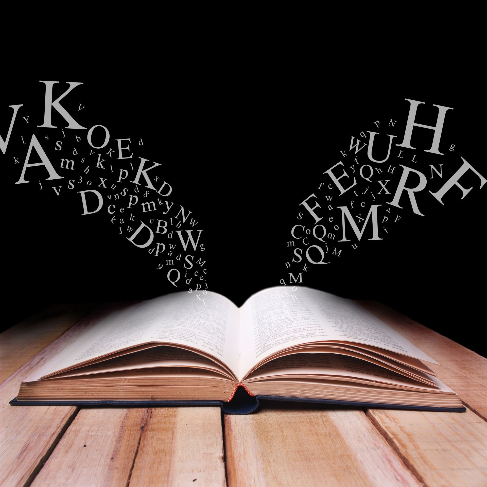 Educational concept. Opened book on wooden table with alphabet letters flying over against black dark background