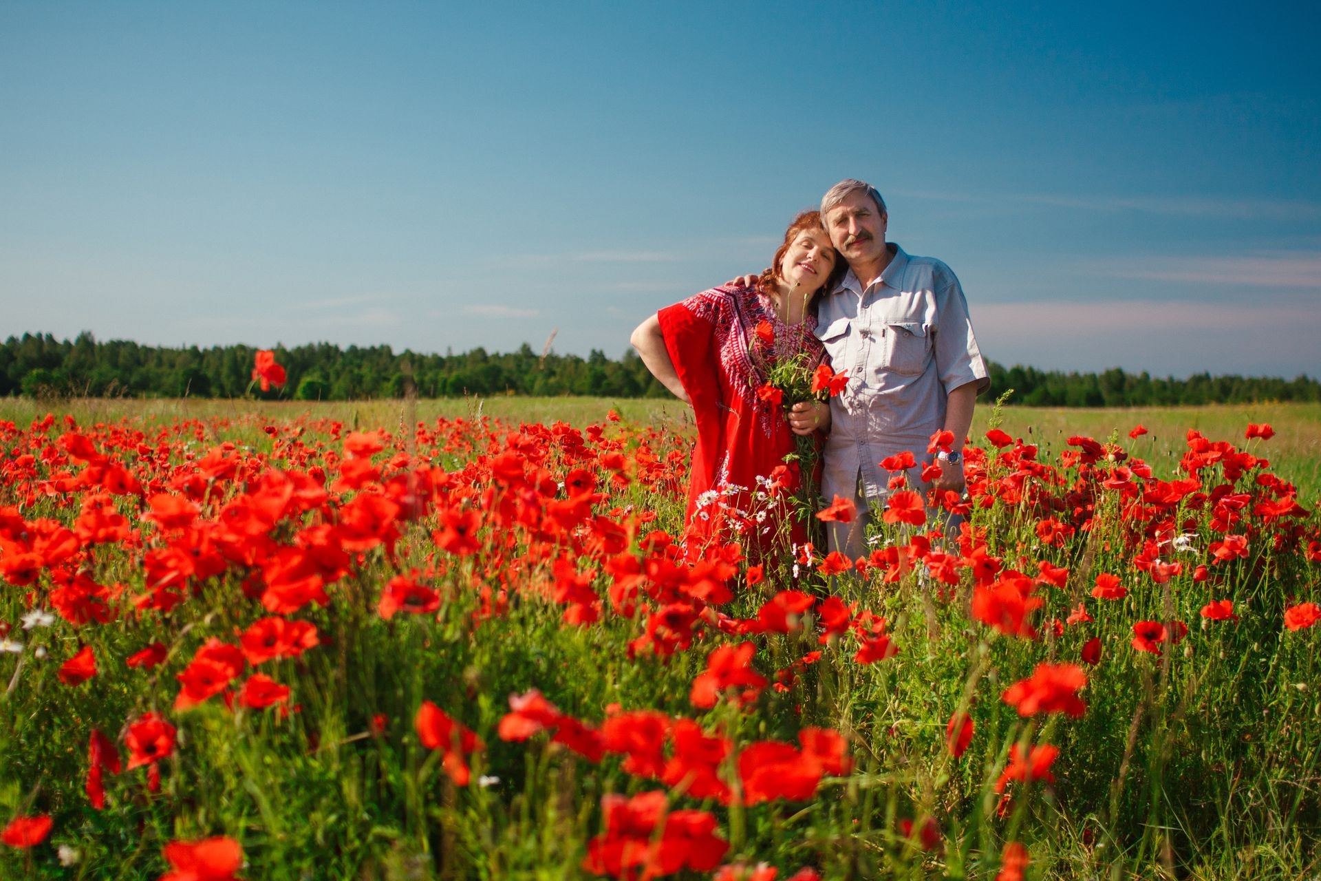 Happy old Elderly couple having fun, walking in a field with poppy flowers. Healthcare lifestyle senior couple relax in spring. People in love in summer time.