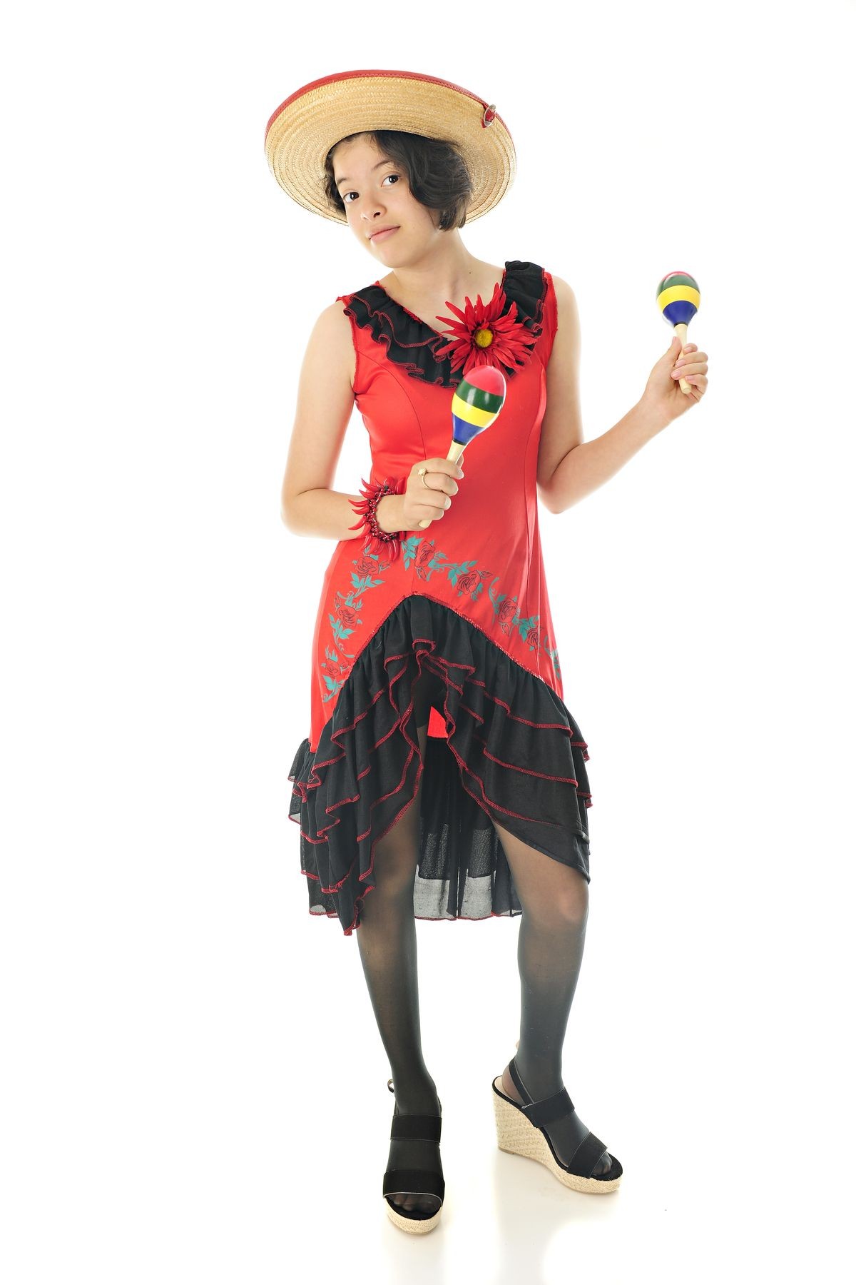 An attractive teen girl dancing with maracas in her red and black Mexican dress and straw sombrero.  On a white background.