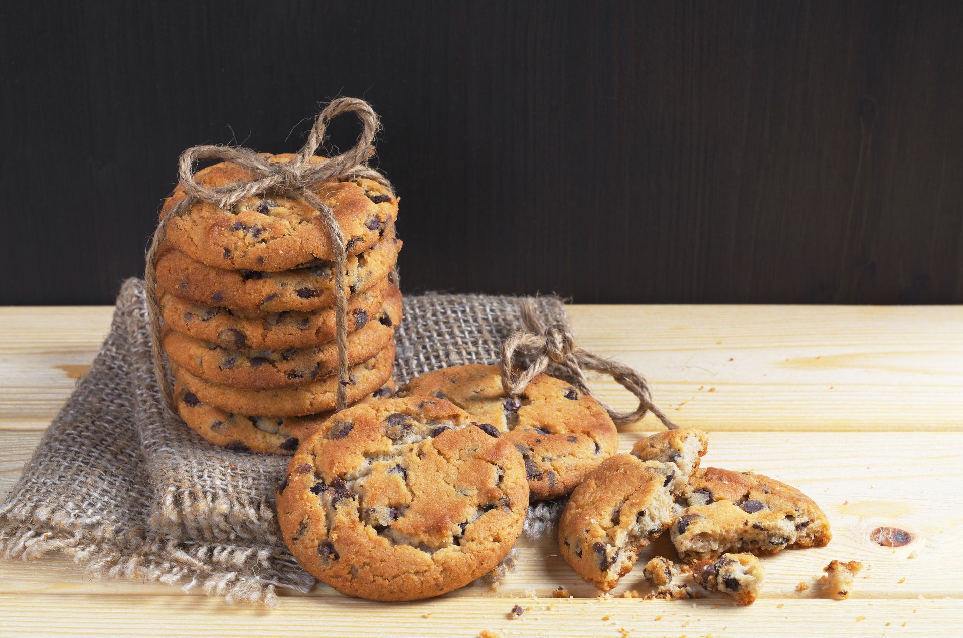 Stack of chocolate chip cookies tied with a rope and half with crumbs on burlap fabric on the wooden table