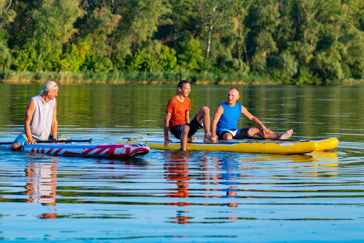 Joyful friends, a SUP surfers relax on the big river during sunset and having fun. Stand up paddle boarding - awesome active outdoor recreation. 