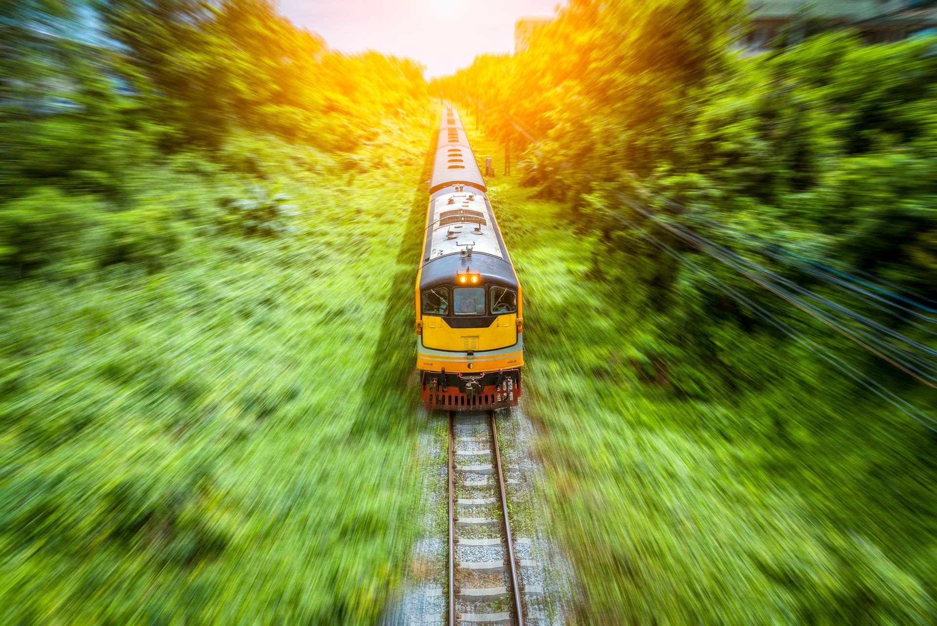 The passenger train speed to train platform by pass green trees nature beside by sunlight rays and blue sky background