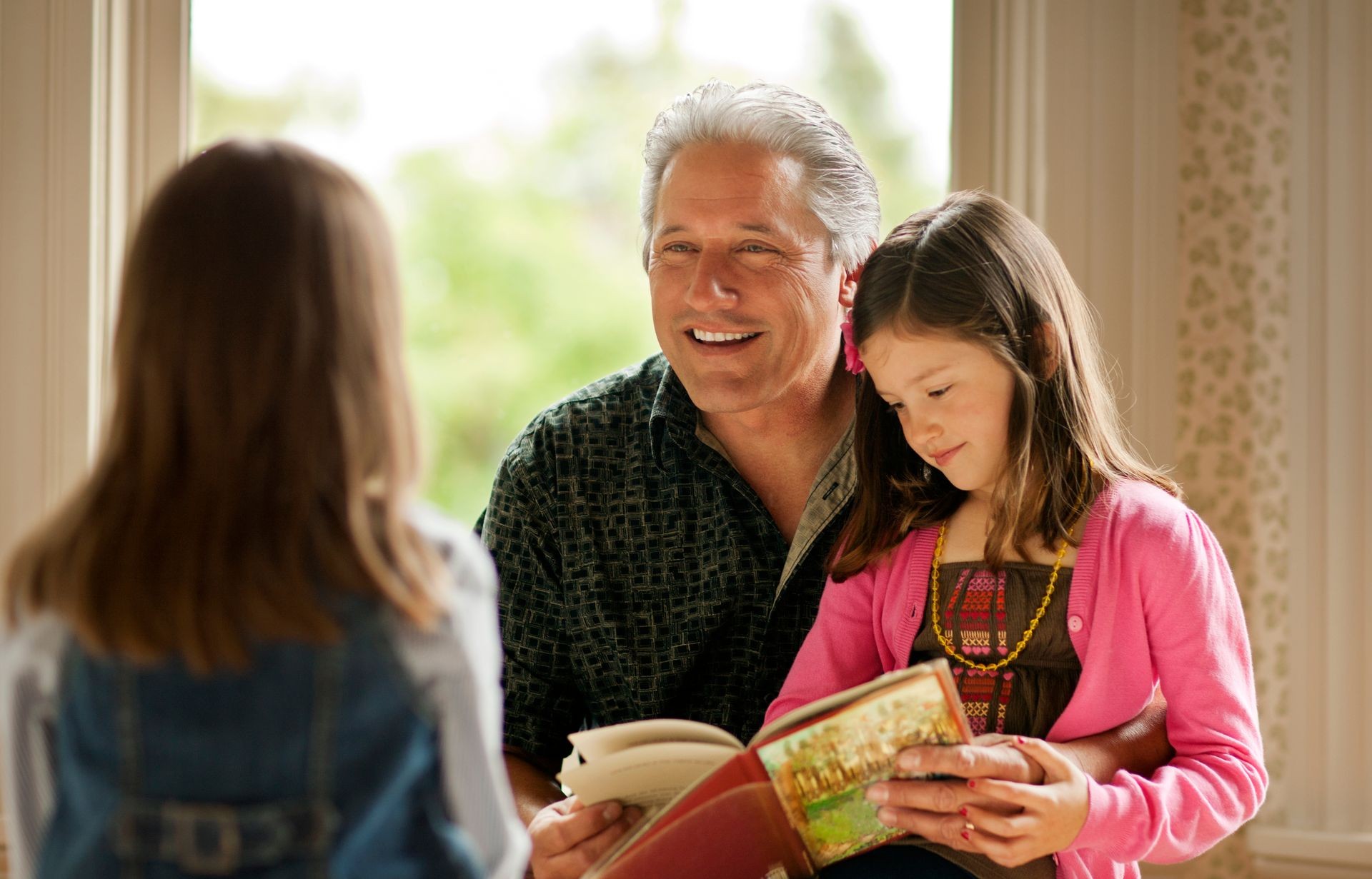 Smiling mid adult man looking at a story book with his young daughter.