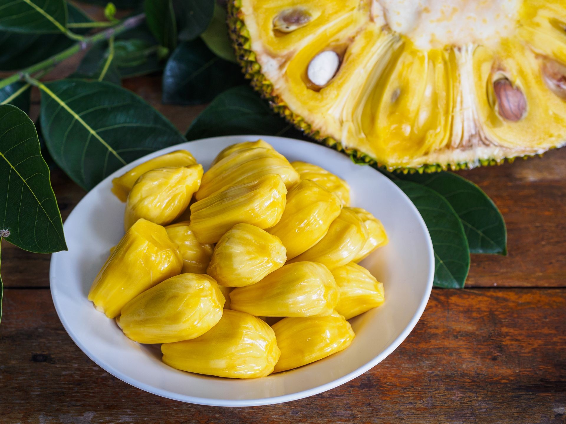 Fresh Jackfruit in white dish, half of jack fruit and jackfruit leaf on wooden table.