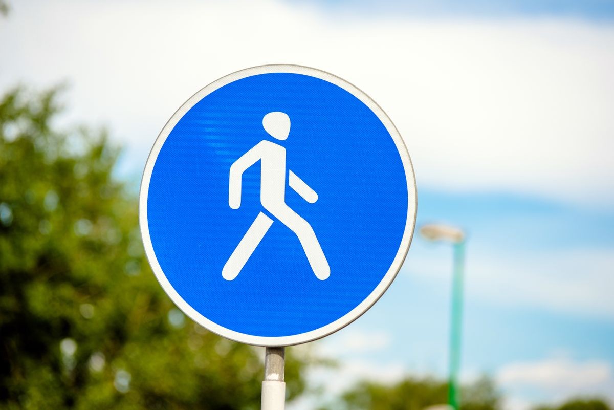 Road sign for pedestrian crossing against blue sky 