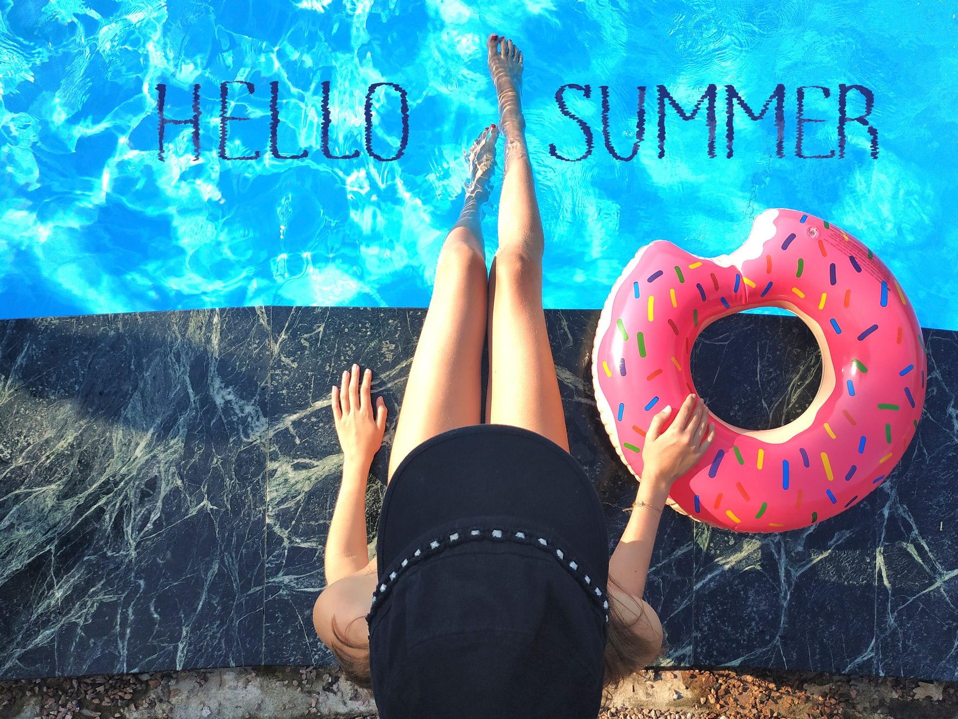 Young woman is relaxing with donut in the swimming pool at spa resort. View from above. Relaxing, vacation, summer holiday idyllic concept. Blue lettering Hello Summer.