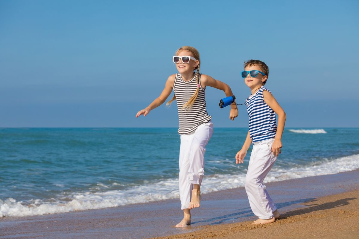 Two happy little children playing on the beach at the day time. They are dressed in sailor's vests. Kids having fun outdoors. Concept of sailors on vacation and friendly family.