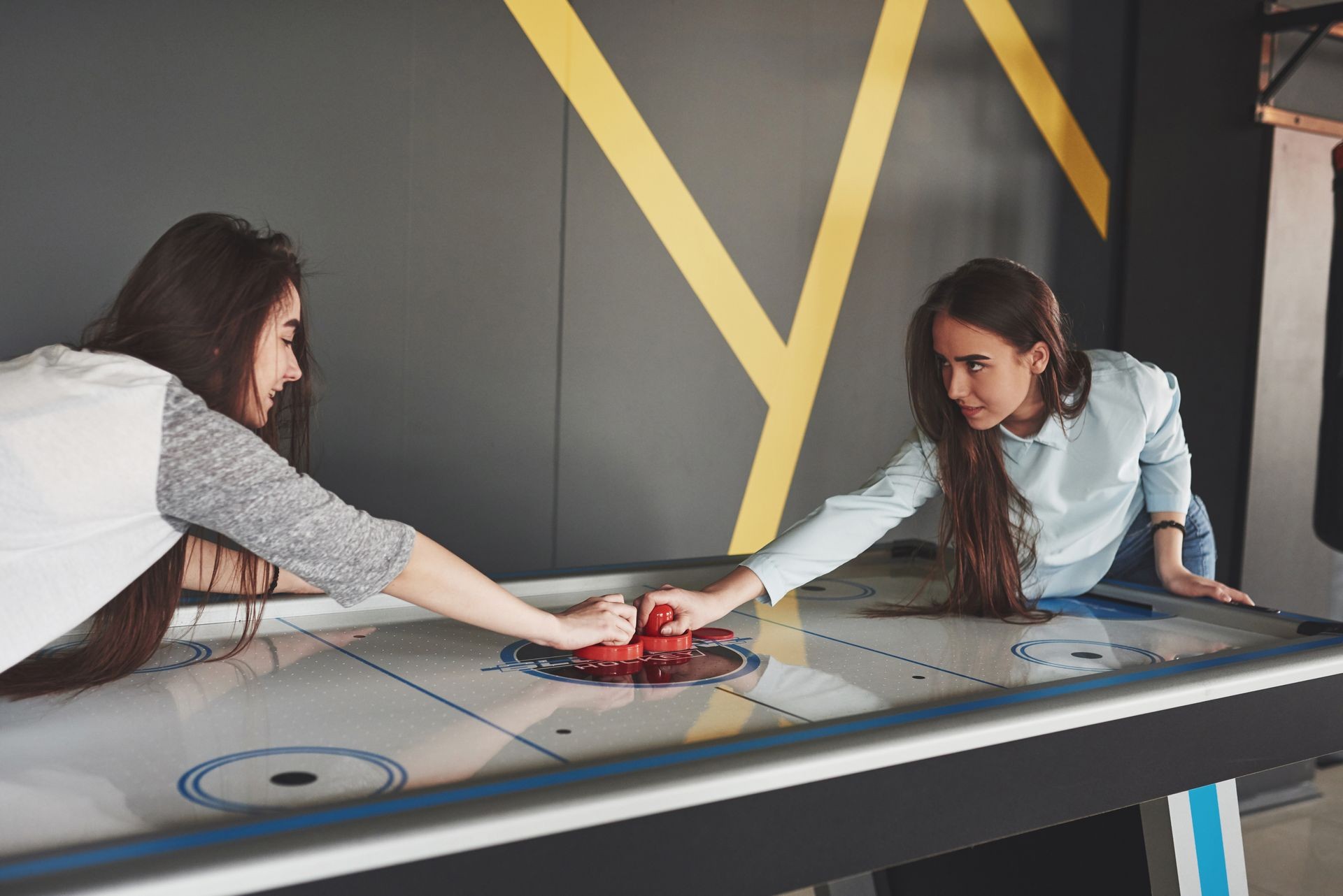 Two beautiful twin girls play air hockey in the game roomand have fun.