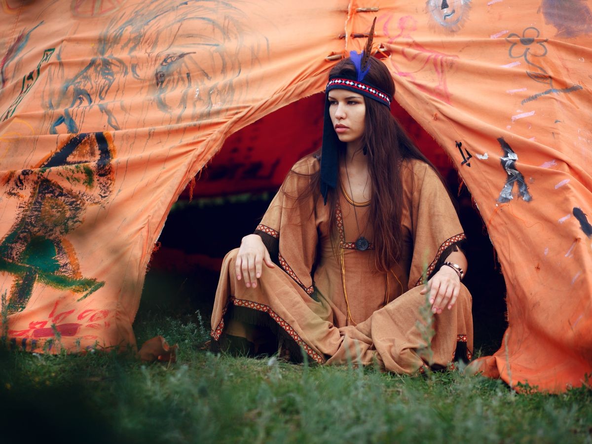 Portrait of a beautiful girl. Indian woman in traditional dress in tent, looking a side, sitting on green grass in summer time.