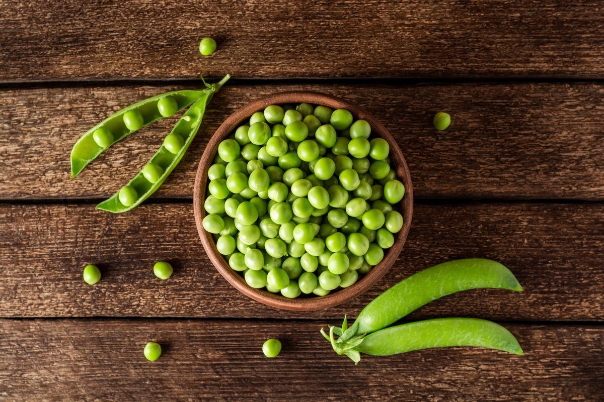 Fresh green peas in ceramic bowl on dark wooden background. Top view.