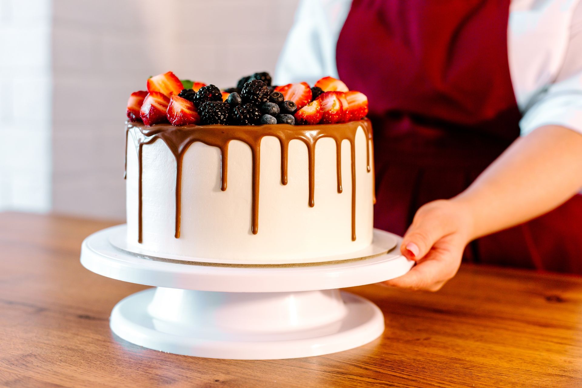 Girl in a red apron holding a birthday cake decorated with fresh berries