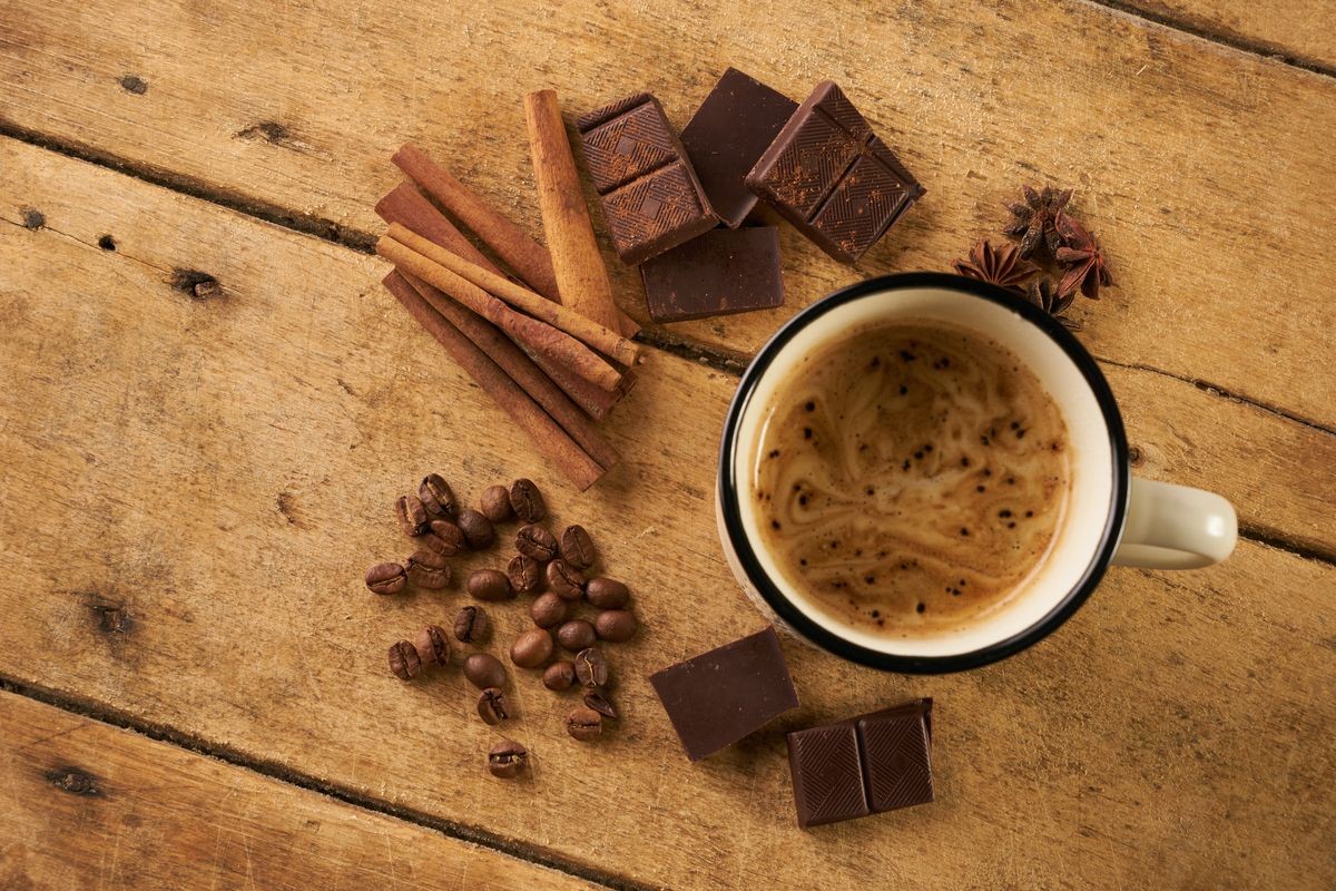 Mug with hot coffee and arabica coffee beans with broken dark chocolate, cocoa powder, cinnamon sticks and anise on wooden rustic table.