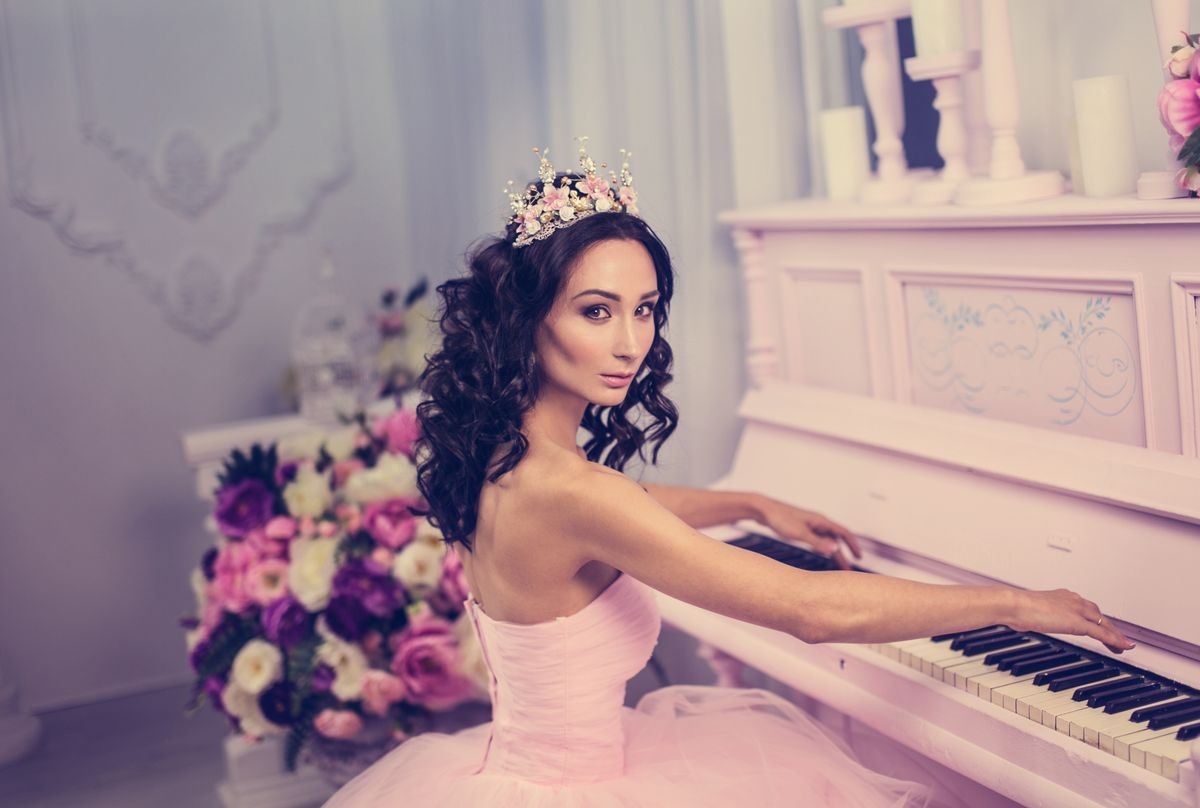 Beautiful girl in a pink dress with a princess crown on pink playing piano