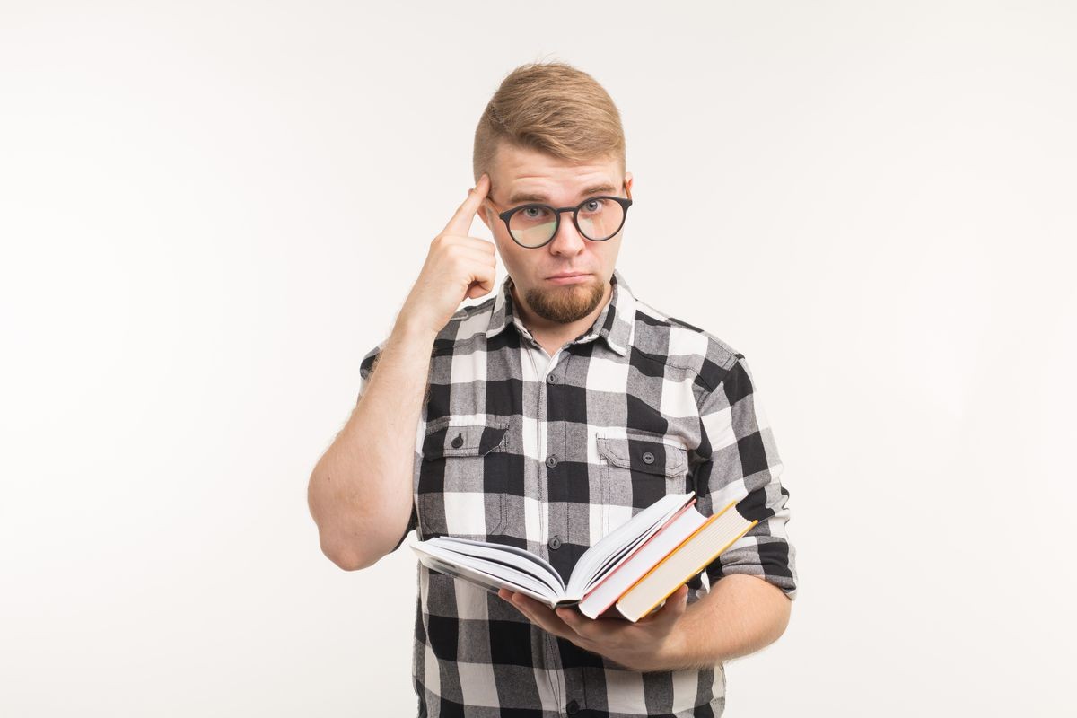 Exam, knowledge and education concept - Smart student man point on head or brain holding books in his hands on white background