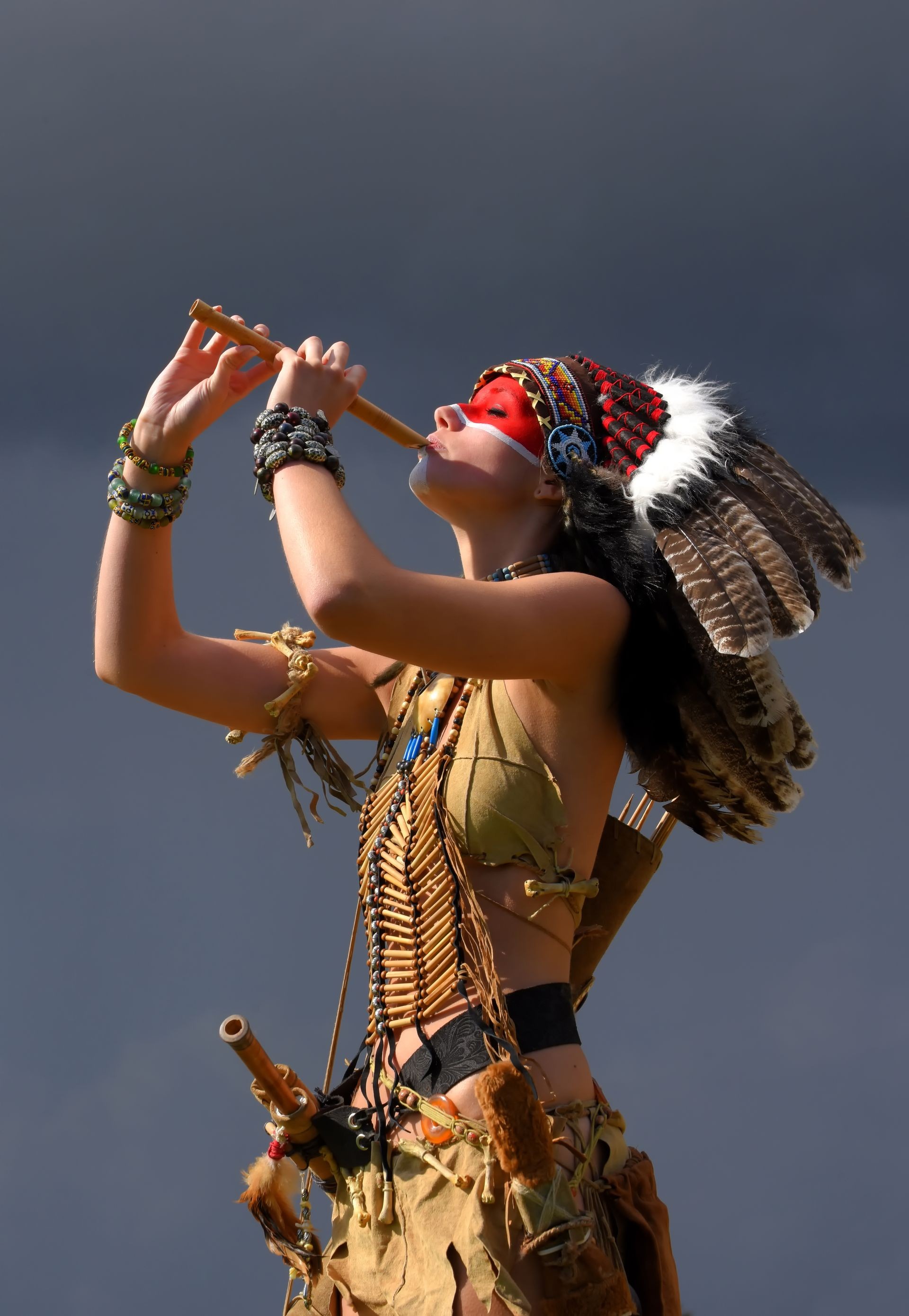 A young girl plays the part of a native American Indian 
girl. Dressed as a native Indian wearing a feathered 
headdress. She poses outdoors in a nature surrounding.