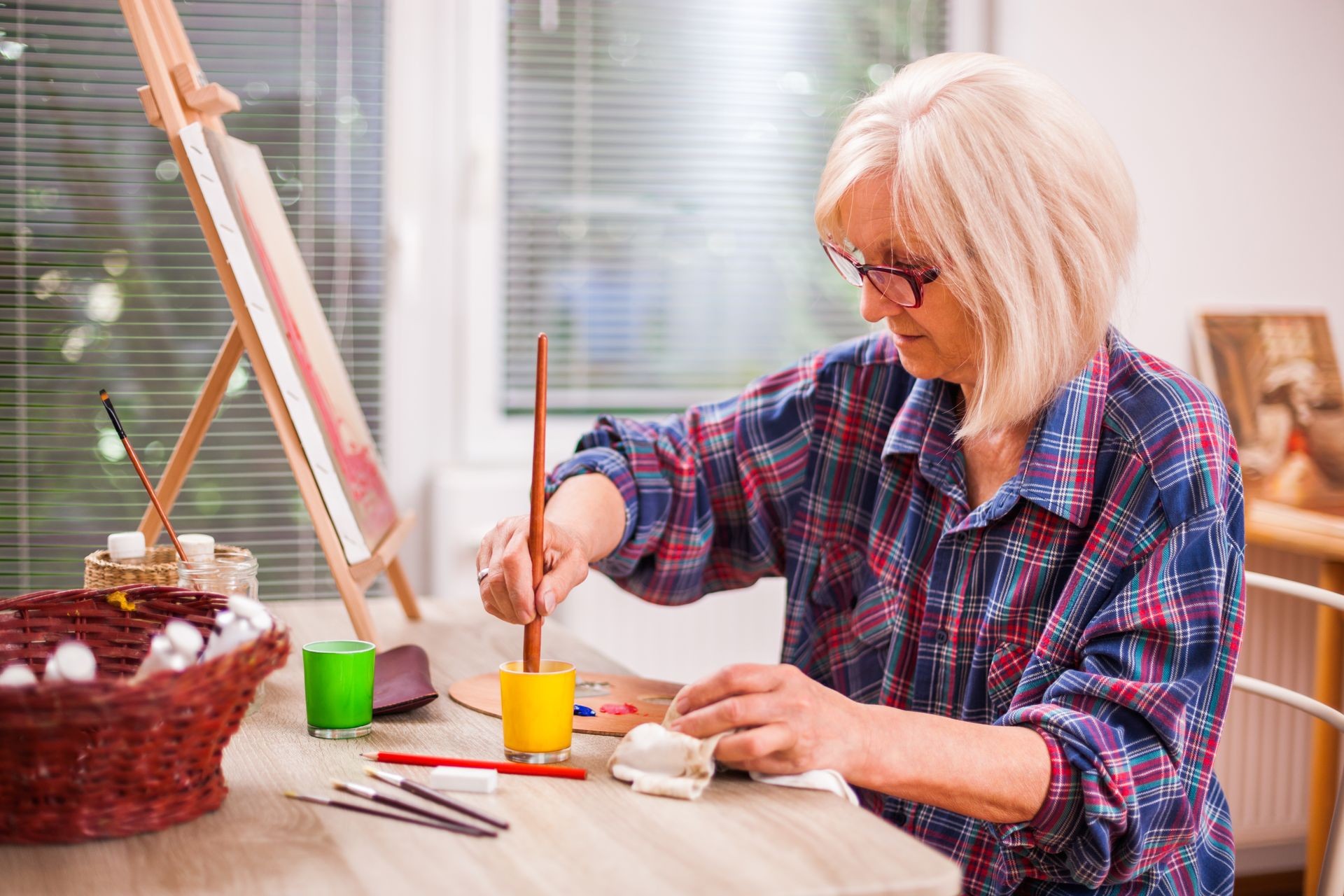 Elderly woman is painting in her home. Retirement hobby. 