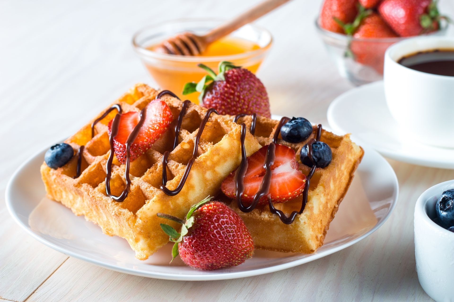 Fresh homemade food of berry Belgian waffles with honey, chocolate, strawberry, blueberry, maple syrup and cream. Healthy dessert breakfast concept with juice