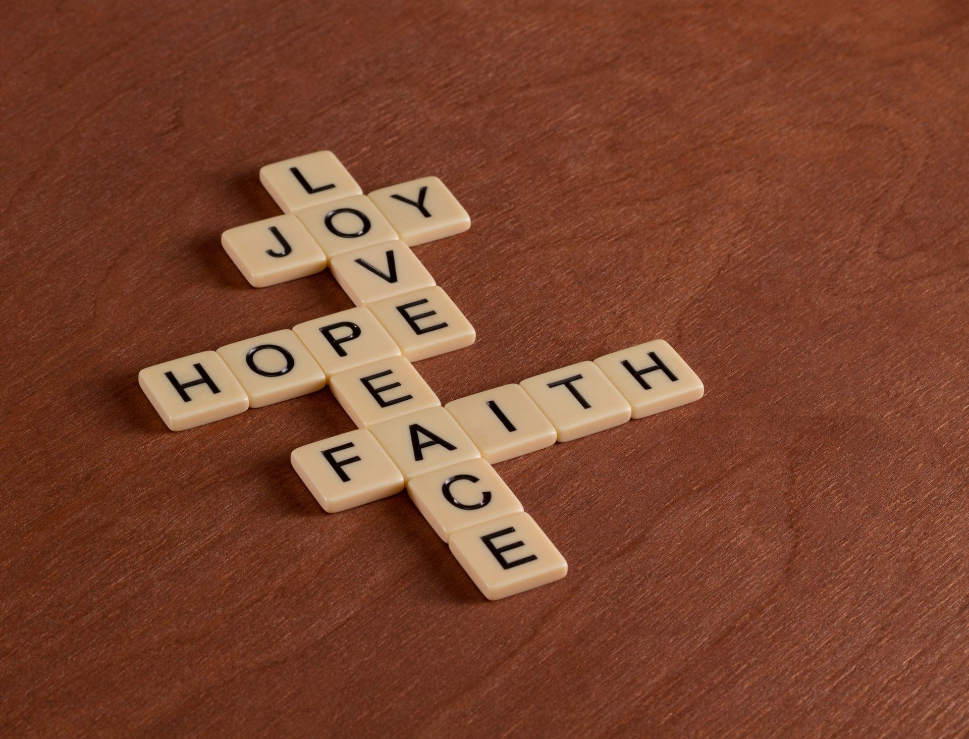 Crossword puzzle with words Faith, Hope, Love. Faith concept. Ivory tiles with capital letters on mahogany board.